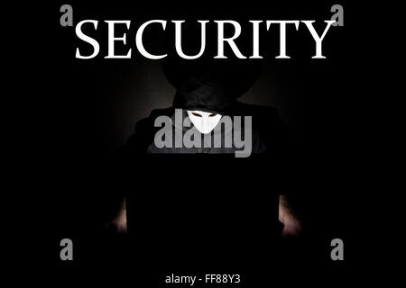 Un homme masqué à un ordinateur portable symbolisant les dangers de l'Internet. Banque D'Images