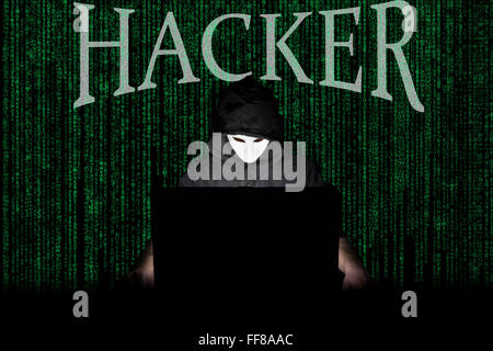 Un homme masqué à un ordinateur portable symbolisant les dangers de l'Internet. Banque D'Images