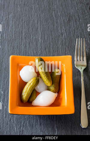 Oignons et cornichons pellicule dans un petit bol en verre sur un fond ardoise foncé Banque D'Images