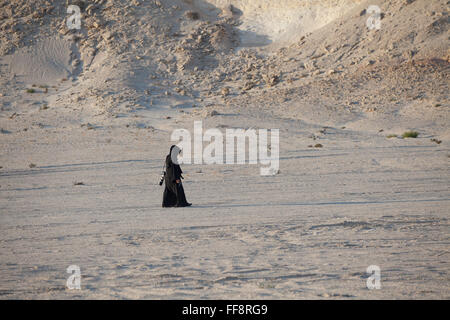 Lone femme arabe marche dans Brouq, Réserve naturelle du désert du Qatar en vêtements traditionnels, l'abaya, près d'un plateau de gypse. Banque D'Images