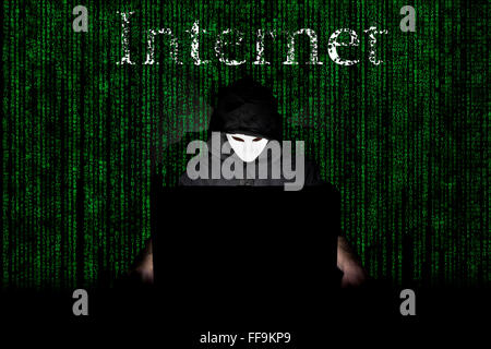 Un homme masqué à un ordinateur portable symbolisant les dangers de l'Internet. Banque D'Images