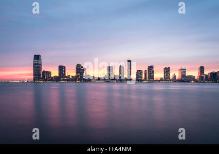 Un magnifique coucher de soleil sur les gratte-ciel de Jersey City et de la rivière Hudson, avec le ciel rose reflète dans l'eau. Banque D'Images