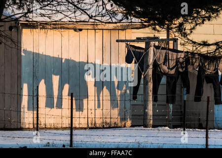 Le séchage des vêtements sur une ligne à l'extérieur en hiver, casting shadows sur le côté du bois d'une maison Amish, Michigan, USA Banque D'Images