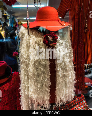 Red Hat d'une femme blanche à froufrous et gilet inhabituelle, qui pourrait être porté comme un foulard-haut, à l'affiche dans la fenêtre d'un magasin de vêtements Banque D'Images