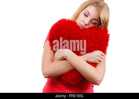 Femme blonde triste malheureux girl hugging grand coussin en forme de coeur rouge, studio shot on white. Navré de jeunes femelles. Banque D'Images