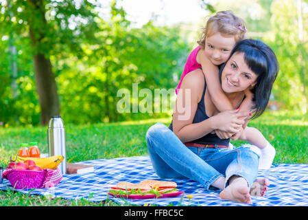 Petite fille étreindre sa mère de vous détendre dans le parc Banque D'Images