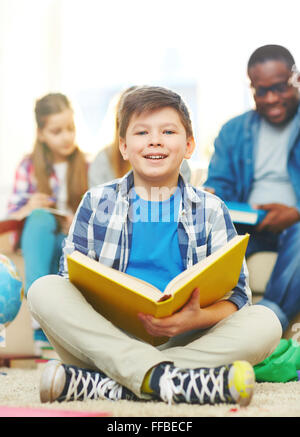 Cute schoolboy avec livre ouvert looking at camera Banque D'Images