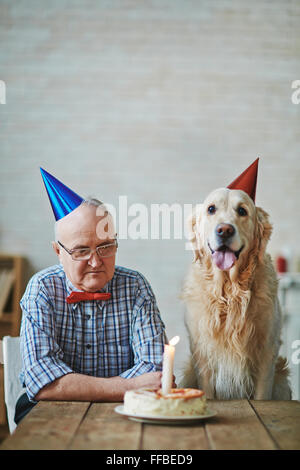 Homme mature et son animal assis par table avec gâteau d'anniversaire avec les bougies Banque D'Images