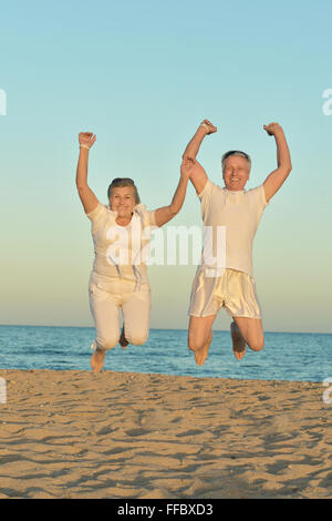 Mature couple jumping on beach Banque D'Images