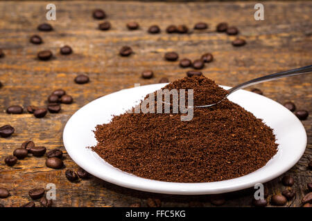 Café moulu sur plaque blanche avec cuillère et entourant les grains de café Banque D'Images