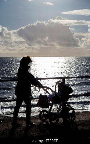 Maman avec la pram à marcher le long du front de mer en hiver silhouette Banque D'Images