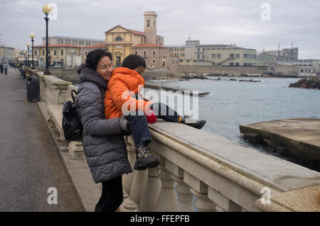 Livorno, Italie. Caucasian woman aide son Amérique adopté boy pour traverser une frontière maritime. La saison d'hiver Banque D'Images
