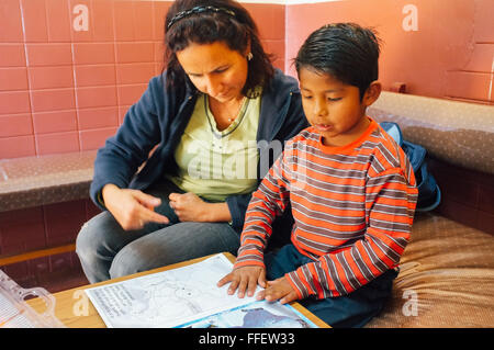 Young caucasian woman aide sa a adopté l'enfant avec ses devoirs lecture tandis que Robin des Bois à l'orphelinat Banque D'Images
