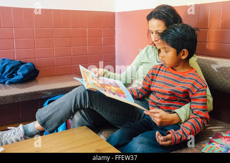 Young caucasian woman aide sa a adopté l'enfant avec ses devoirs lecture tandis que Robin des Bois à l'orphelinat Banque D'Images