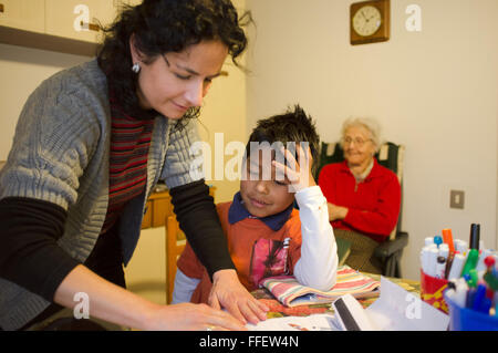 Young caucasian woman aide sa a adopté l'enfant avec ses devoirs pendant que grand-mère regarde en souriant sur une chaise fermer Banque D'Images