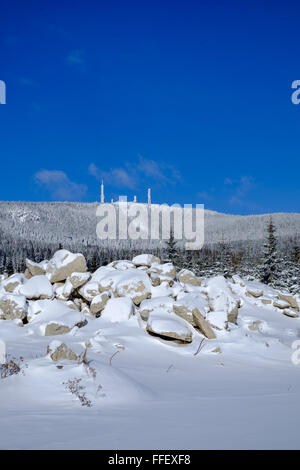 Un paysage hivernal avec des rochers enneigés au premier plan et Harghita Mountain avec des antennes de télécommunication en arrière-plan. Banque D'Images