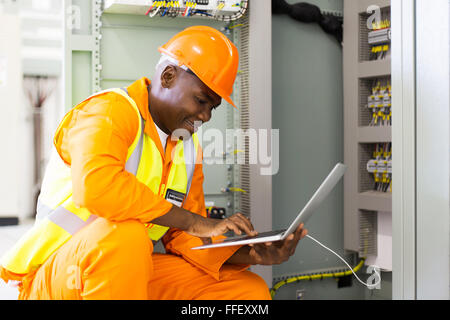 Jeune ingénieur américain africain à l'aide d'ordinateur portable dans la salle de commande de la machine Banque D'Images