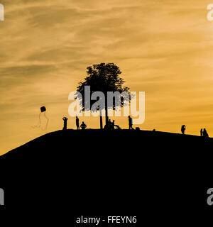 Silhouettes de personnes sur une colline, l'arbre et une personne voler un cerf-volant au crépuscule Banque D'Images