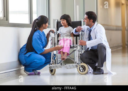 Jeune enfant de sexe féminin patient in wheelchair sitting in hospital corridor avec femmes asiatiques et indiennes infirmière médecin homme Banque D'Images