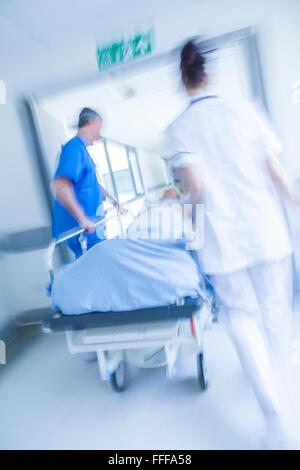 Une photographie d'un flou de mouvement senior female patient sur civière ou gurney poussés en pleine vitesse dans un couloir de l'hôpital Banque D'Images