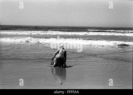 Jan 4, 2016 - South Beach, KwaZulu-Natal, Afrique du Sud - une femme s'agenouille sur le sable humide, la collecte de l'eau de mer pour l'auto-guérison. South Beach est une partie de la ville de Durban sans interruption la plus longue étendue de plage de sable. La ville de Durban est sur la côte est de l'Afrique du Sud et les gens ici sont lavés avec de l'eaux chaudes de l'Océan Indien. Au nord de cette étendue de sable sont des plages avec la société hang out cafe. Au sud il y a une jetée avec le quartier haut Moyo's Restaurant à elle est la fin et l'uShaka Marine World et le secteur complexe de la mer et surf clubs de la vesces Banque D'Images