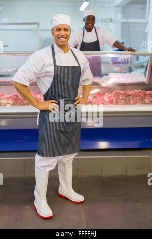 Boucher d'âge moyen posant devant un collègue de travail dans une boucherie Banque D'Images