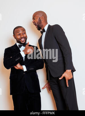 Deux hommes d'afro-américaine en costumes noirs qui posent des gestes, émotionnelle, souriant. Le port de liens à l'arc Banque D'Images