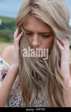 Portrait d'une belle jeune fille avec de longs cheveux blonds tenant sa tête dans ses mains Banque D'Images