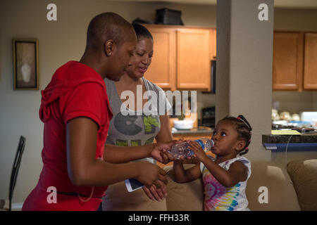 Somaya, 2, fille de sergent. Chantel Thibeaux, Base-Fort mixte Sam Houston, Texas, assistant dentaire, de l'instructeur se tient sur le canapé tandis que sa mère et sa grand-mère Carla regarder son verre d'eau. À deux ans, Somaya est pas au courant de son combat contre le cancer et les mères ont essayé de jouer avec elle toutes les chances qu'elle peut, mais est limité à certaines activités. Environ 15 parents et amis réunis chez elle pour célébrer le succès de la chirurgie et de fournir l'amour à Thibeaux au cours de sa quête pour vaincre le cancer. Banque D'Images