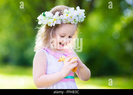 Petite fille s'amusant sur chasse aux œufs de Pâques. Kid en jouant avec la couronne de fleurs canard ou poulet. Les enfants à la recherche d'oeufs Banque D'Images