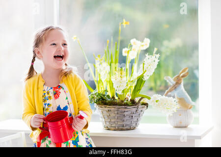 Cute girl premier arrosage de fleurs de printemps. Intérieur et décoration Accueil Pâques. Enfant en prenant soin des plantes. Kid avec de l'eau peut. Banque D'Images