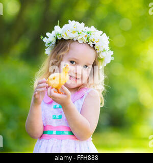 Petite fille s'amusant sur chasse aux œufs de Pâques. Kid en jouant avec la couronne de fleurs canard ou poulet. Les enfants à la recherche d'oeufs Banque D'Images