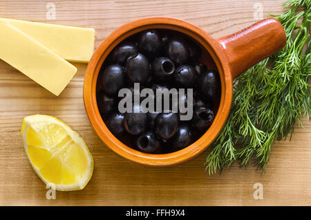 Dans une tasse d'olives noires, fromage, une tranche de citron et aneth sur table en bois Banque D'Images