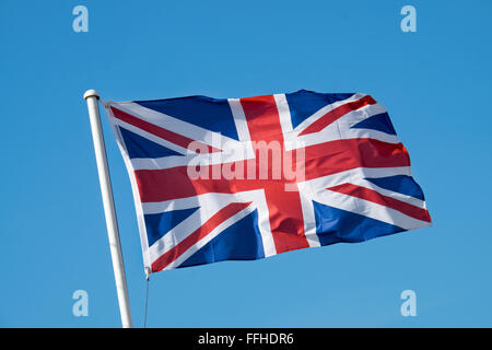 L'union flag fluttering au sommet d'un mât blanc sur une journée ensoleillée contre un ciel bleu clair Banque D'Images