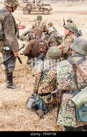 Seconde guerre mondiale re-enactment. Groupe de soldats allemands Waffen SS, en point motif camouflage, assis et attendant dans l'herbe jaune. Banque D'Images