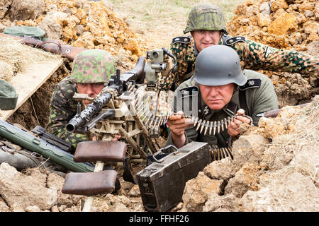 Seconde Guerre mondiale re-enactment. Deux hommes Waffen SS des uniformes de camouflage, derrière la machine gun avec canon en direction de spectateur. Close-up. Banque D'Images