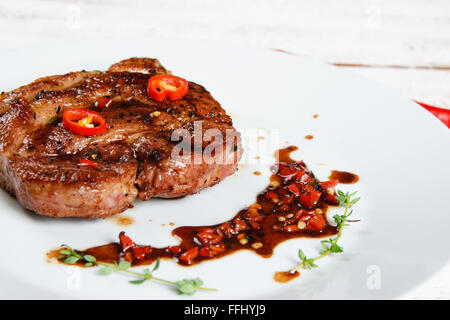 Steak sur une plaque blanche avec sauce rouge épicée. Le point de droit. Banque D'Images