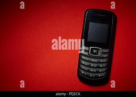 Vieux téléphone cellulaire noir sur le fond rouge. Banque D'Images
