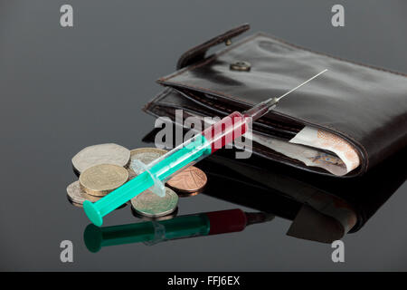 Rempli de sang pose de l'autre côté d'une aiguille hypodermique trésorerie lâche et un portefeuille sur un arrière-plan sombre reflet Banque D'Images