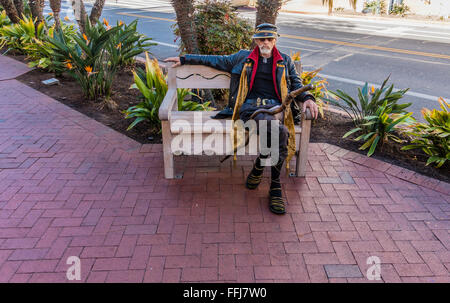 Une personne âgée, rue excentrique personnage est assis sur un banc public sur la State Street avec son grand bâton de marche et une tenue étrange Banque D'Images