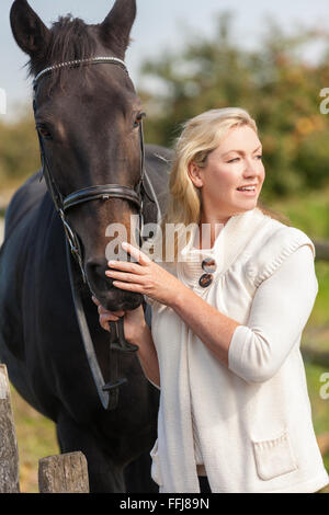 Beautiful happy young woman smiling et caresser son cheval à l'extérieur dans le champ ensoleillé Banque D'Images