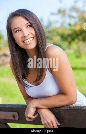 Belle jeune femme asiatique ou eurasienne girl wearing white t-shirt, souriant et s'appuyant sur une clôture en sunshine Banque D'Images