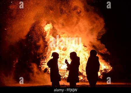 Eriskirch, Allemagne. Feb 13, 2016. Trois jeunes filles se tenir en face d'un feu En Eriskirch, Allemagne, 13 février 2016. La 49e Eriskirch bonfire est un événement traditionnel qui est fait d'environ 300 arbres accumulée sur une période de neuf mètres de haut talon. Photo : Felix Kaestle/dpa/Alamy Live News Banque D'Images