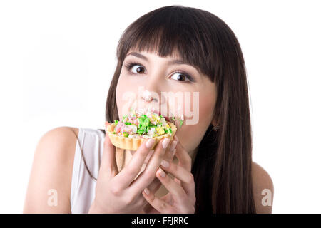Belle jeune femme très faim manger délicieux gâteau tarte avec couverts en crème visage. Panne alimentation concept. Studio Banque D'Images