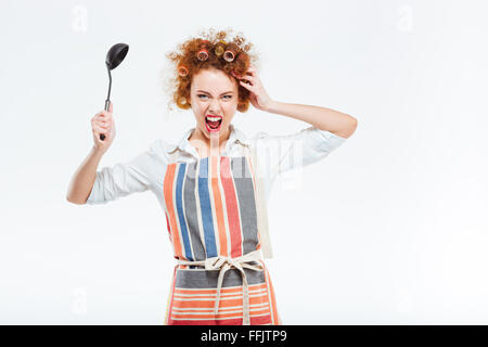 Crazy rousse avec les cheveux bouclés apron holding une louche et criant isolé sur fond blanc Banque D'Images