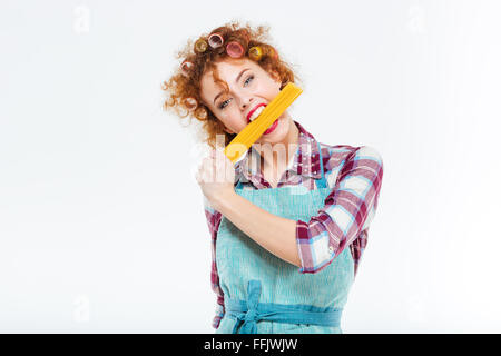 Jolie rousse femme au foyer dans la cuisine tablier, debout et posant avec spaghettis non cuits sur fond blanc Banque D'Images