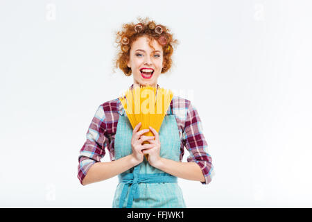 Heureux jolie jeune femme au foyer en chemise à carreaux et tablier bleu debout et tenant spaghettis non cuits sur fond blanc Banque D'Images