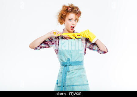 Belle jeune femme au foyer ludique avec les cheveux bouclés rouge posant avec des gants jaune sur fond blanc Banque D'Images