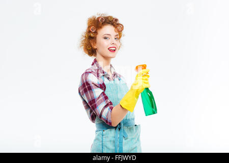 Smiling cute rousse jeune femme au foyer dans les gants en caoutchouc et la pulvérisation bouteille nettoyage holding sur fond blanc Banque D'Images