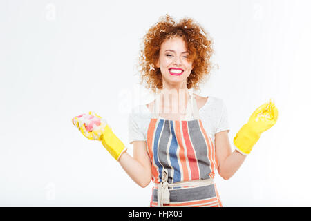 Jeune femme gaie avec de la mousse sur ses cheveux roux bouclés dans les gants en caoutchouc éponge jaune holding et la vaisselle sur fond blanc Banque D'Images